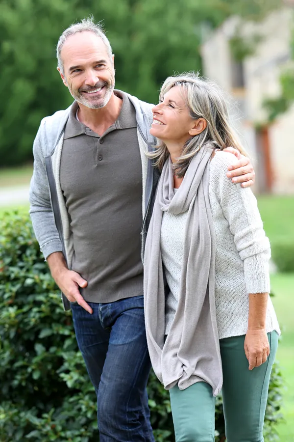 Bioidentical-Hormone-Therapy-Treatment A mature couple in gray toned clothes and jeans walk happily outside, happy with their successful bioidentical hormone treatments from Blessed Beauty Boutique in Greater Phoenix.