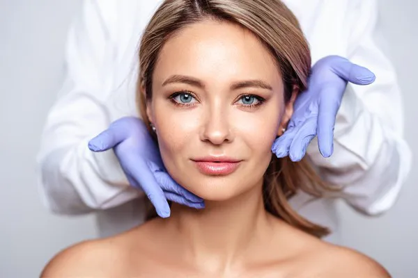 Botox-Doctor Close up of a woman's face with a doctor wearing rubber gloves standing behind her holding his hands around her face to show the amazing Botox Cosmetic treatment from Blessed Beauty Boutique in Greater Phoenix.