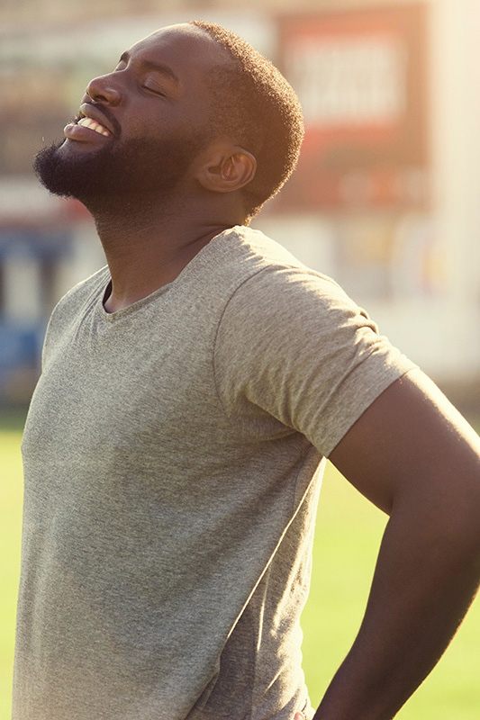 Lean-Muscle-and-Recovery-Treatment A black man in a gray t-shirt and smiles, looking up with closed eyes after a satisfying workout. Get treatment for lean muscle loss and recovery from Blessed Beauty Boutique in Greater Phoenix.