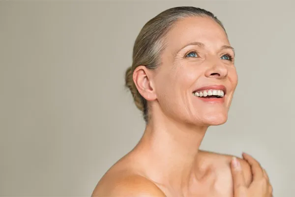 Microdermabrasion-Clinic A beautiful mature woman with her hair tied back wmiling. Get microdermabrasion treatment from Blessed Beauty Boutique in Greater Phoenix.