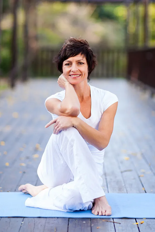Osteoporosis-Treatment A middle-aged woman happily sits in a yoga pose. Get Osteoporosis treatment from Blessed Beauty Boutique in Greater Phoenix.