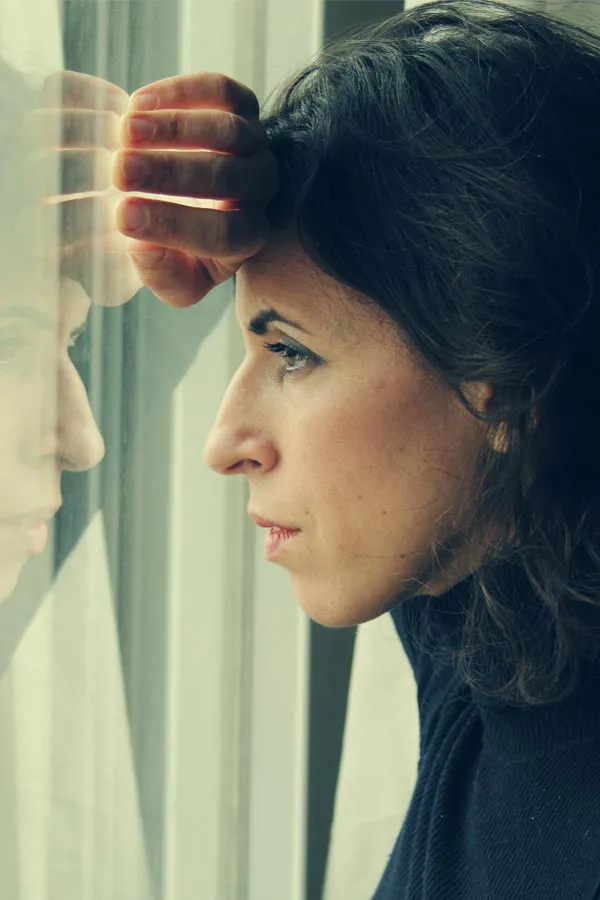 PCOS-Treatment A brunette woman in a thin dark turtleneck looks out the window with a serious expression, suffering from PCOS. Get treatment for Polycistic Ovarian Syndrome/PCOS from Blessed Beauty Boutique in Greater Phoenix.