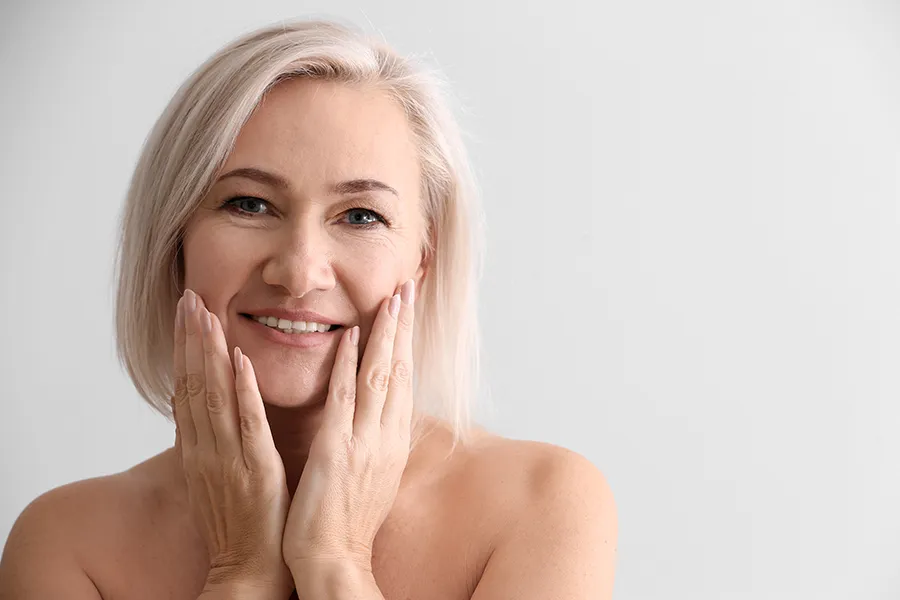 PRP-Microneedling-Clinic A mature woman touches her faces to feel the successful results of PRP microneedling and skin rejuvenation treatments from Blessed Beauty Boutique in Greater Phoenix.