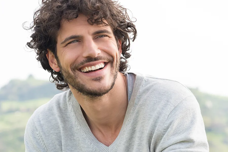 ProCell-Hair-Restoration-Clinic A man with full, long curly hair sits outside smiling. Get ProCell therapy for hair restoration from Blessed Beauty Boutique in Greater Phoenix.
