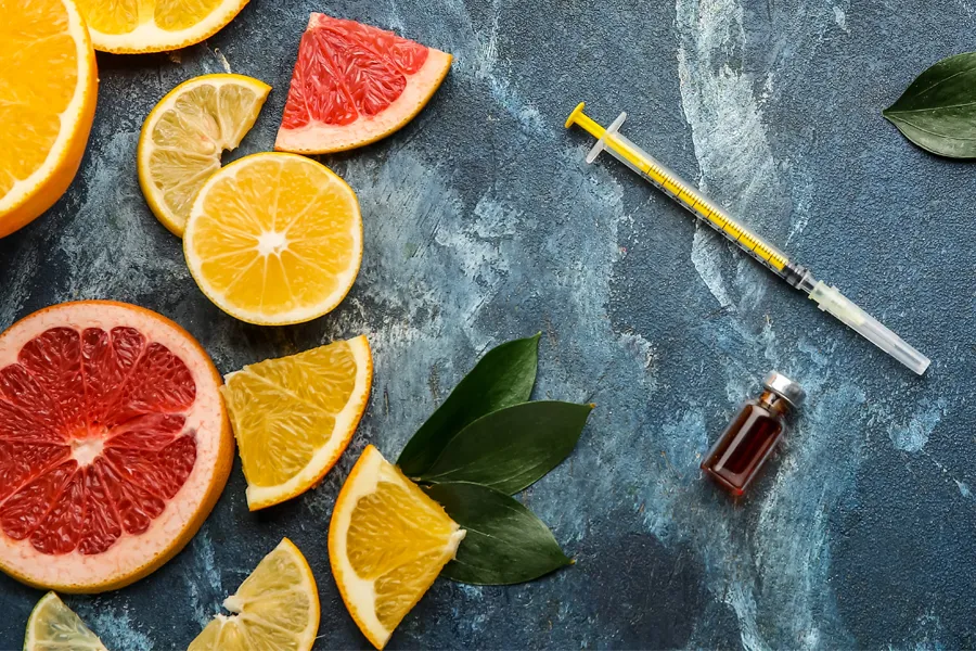Vitamin-Injection-Doctor A gray marble countertop covered with sliced fruit and a syringe and vial, representing vitamin injections from Blessed Beauty Boutique in Greater Phoenix.