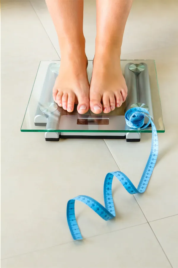 Weight-Loss-Resistance-Treatment Close-up of a woman's feet standing on a scale, with measuring tape by her toes, getting treatment for weight loss resistance from Blessed Beauty Boutique in Greater Phoenix.